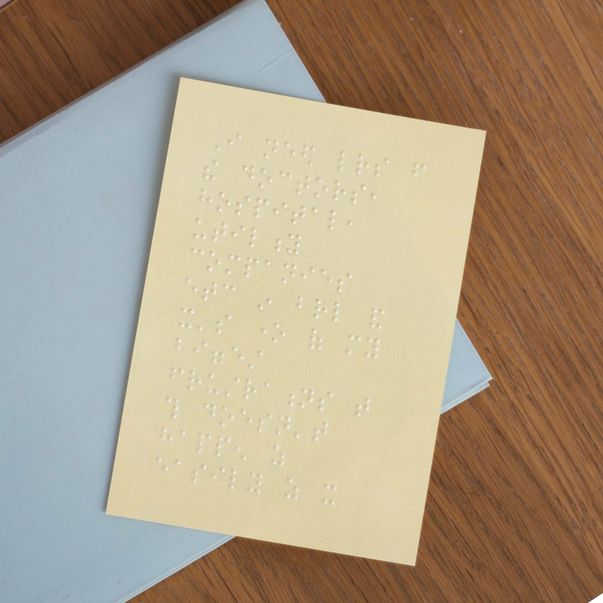 An A6 sheet of braille, the clear adhesive is on yellow backing paper. The sticker is sat on a blue card folder.