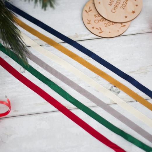 Ribbons in red, green, silver, ivory, gold and navy. At the top of the image you can see two Christmas decorations lay on top of each other, the text is partly covered.