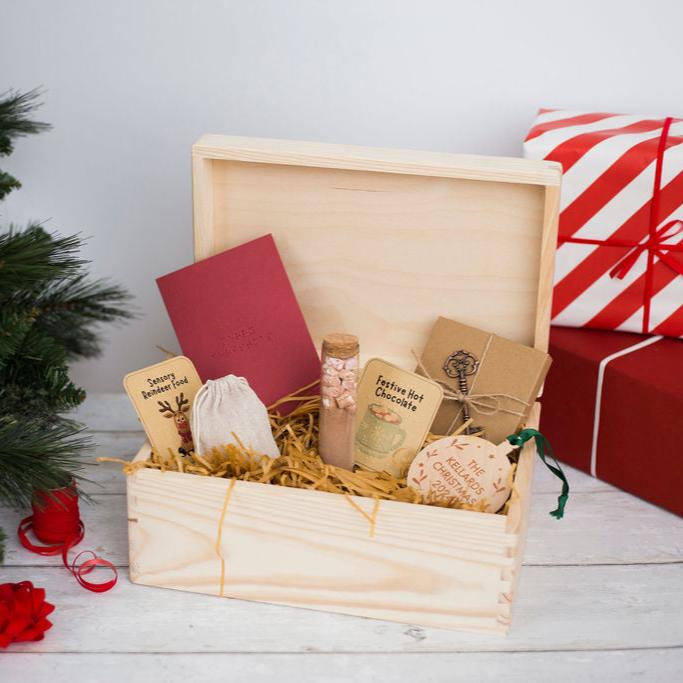 A wooden open Christmas Eve Box filled with various Christmas goodies including hot chocolate, reindeer food, a santa key, a braille Christmas card and a braille Christmas decoration.