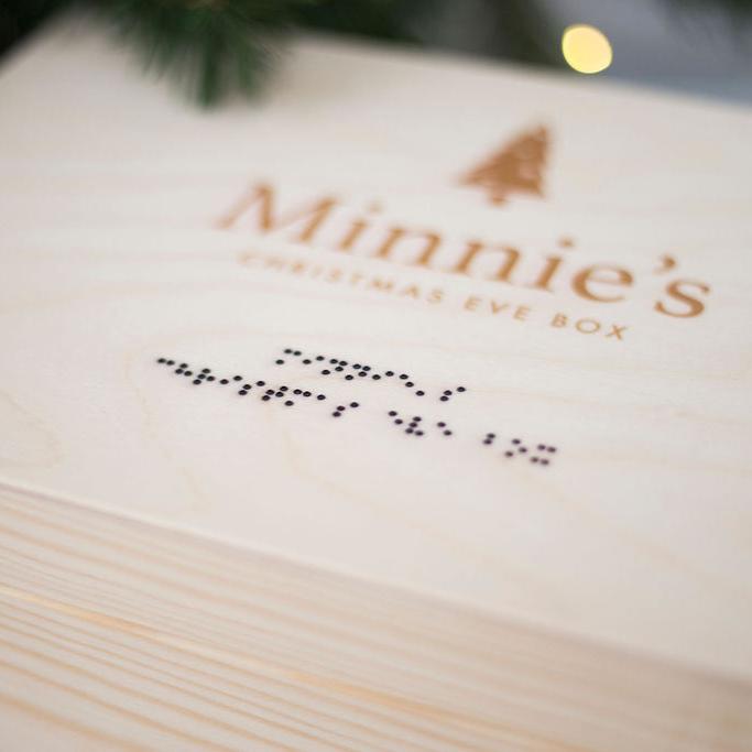 A close up of a Wooden Christmas Eve Box showing the braille which reads Minnie's Christmas Eve Box in lower case grade one braille.