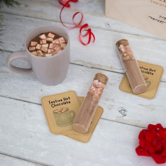 Glass tubes of hot chocolate and marshmallows, with a mug of hot chocolate and marshmallows, and labels saying festive hot chocolate in both print and braille.