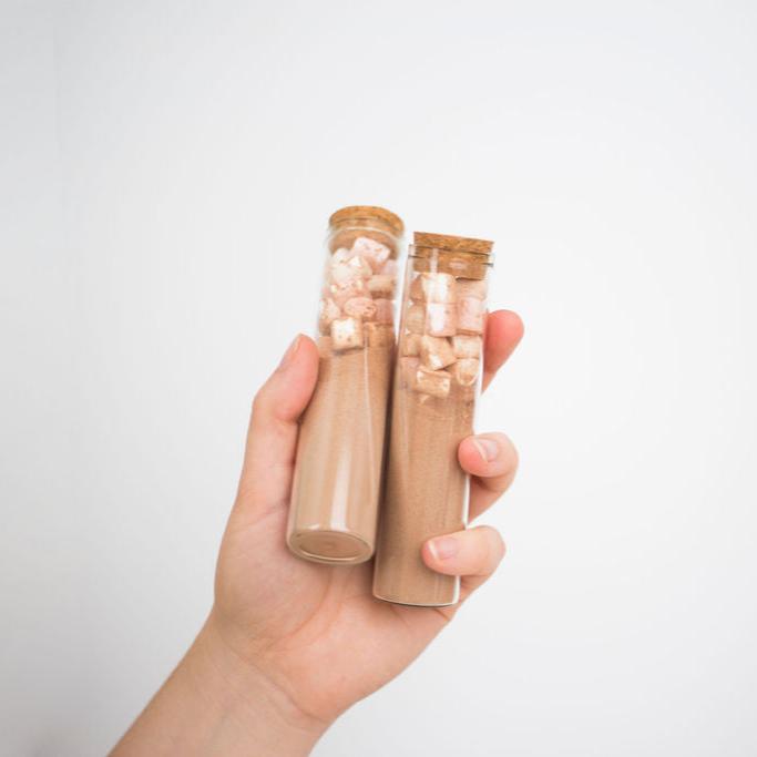 A hand holding two glass tubes of hot chocolate with marshmallows.