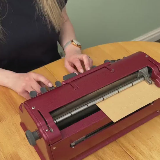 Hayley typing on a red Perkins Brailler.