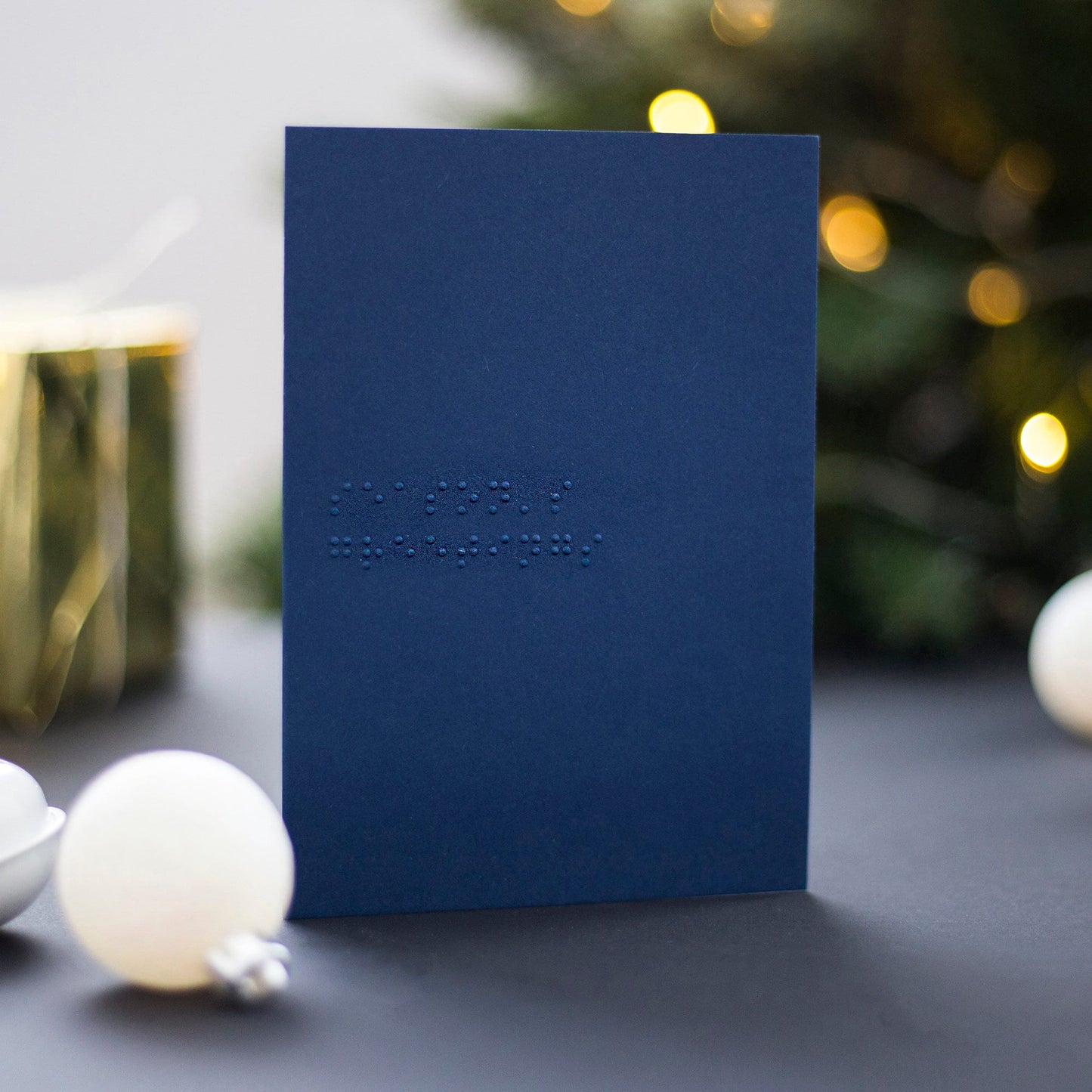 A navy blue braille Christmas card with season&#39;s greetings written in lower case UEB.